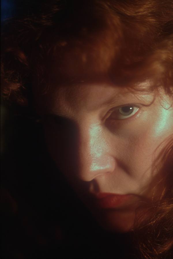 Une femme rousse, le regard de biais, la moitié du visage dans l'ombre